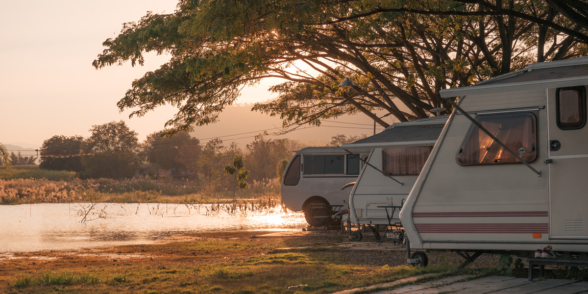 Motor home under big tree on campground by the lake in the evening